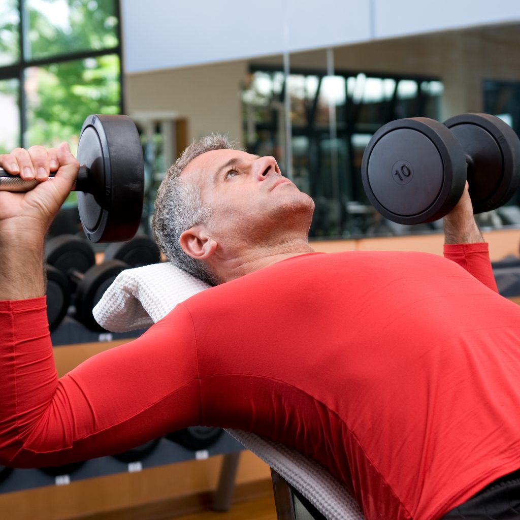 Mature man lifting dumbells at fitness gym